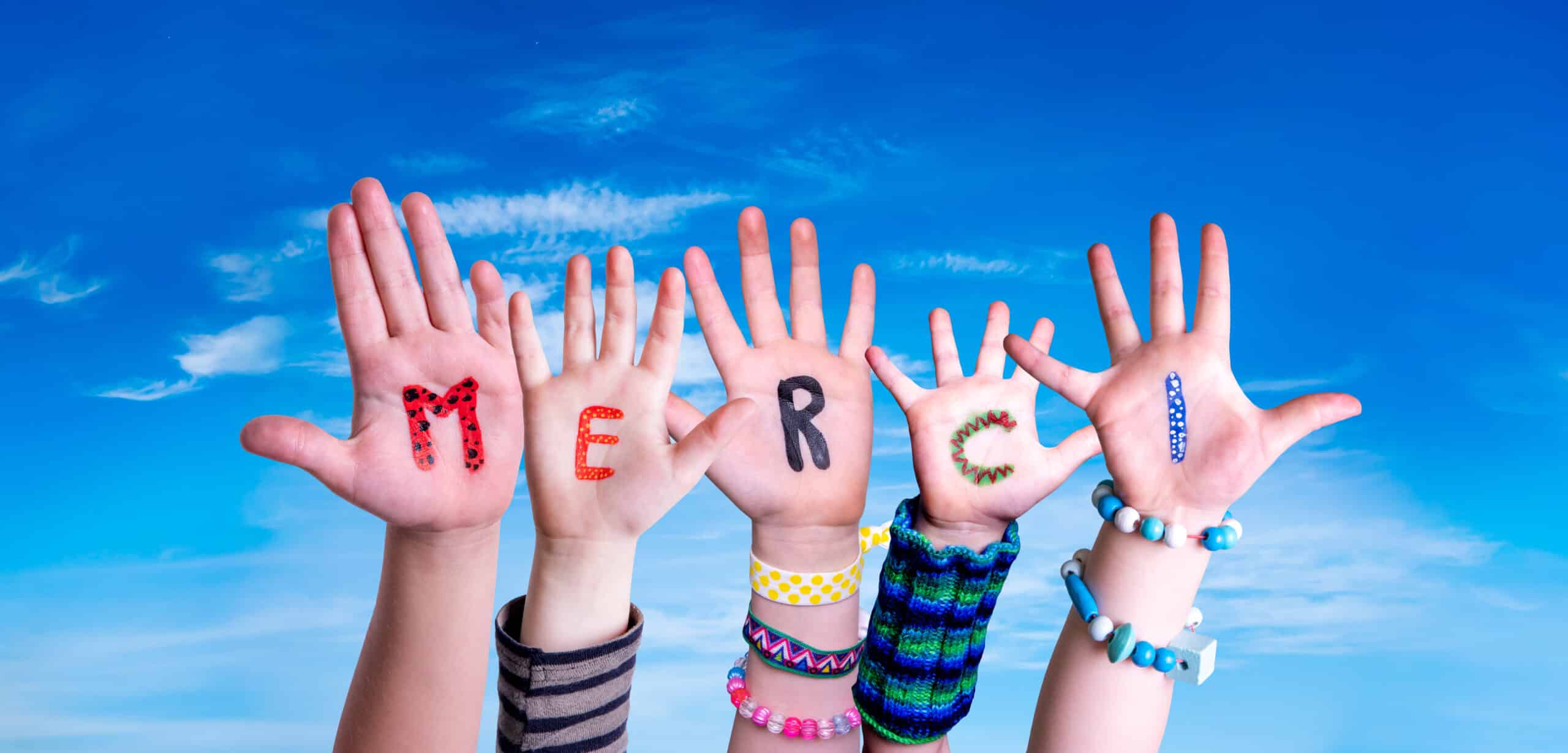 niños creando la palabra en frances Merci que significa gracias. Cielo azul como fondo. niños creando la palabra en frances Merci que significa gracias. Cielo azul como fondo.